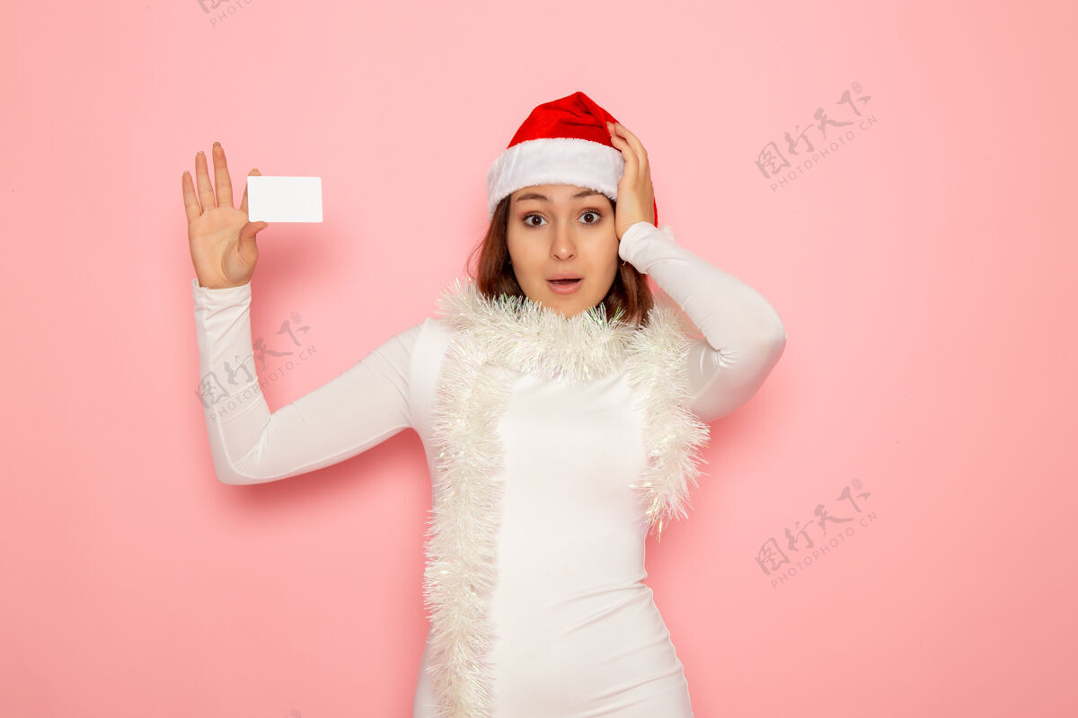 风景正面图年轻女子手持白色银行卡在粉色墙上圣诞假期新年彩钱年轻女性肖像衣服
