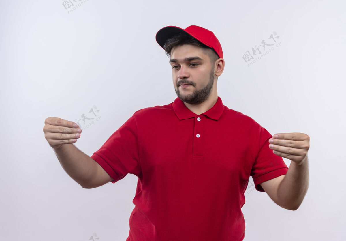 红年轻的送货员穿着红色制服 戴着帽子 自信地用手做手势 肢体语言概念男人姿态看