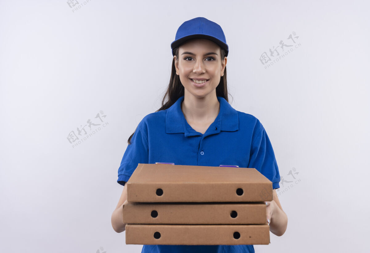 脸身穿蓝色制服 戴着帽子的年轻送货员拿着一叠比萨饼盒 面带自信的微笑看着镜头帽子盒子蓝色