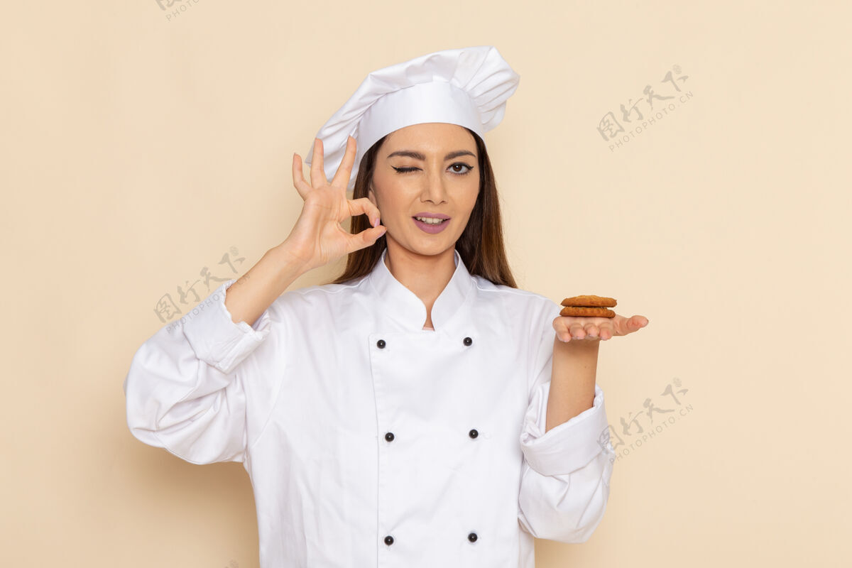 套装身穿白色厨师服的年轻女厨师手持饼干 在浅白的墙上眨眼年轻专业前面