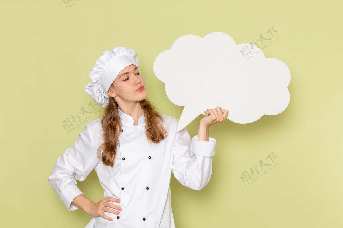 肖像女厨师身穿白色厨师服 手持绿色墙壁上的白色标志的正面图举行烹饪前面
