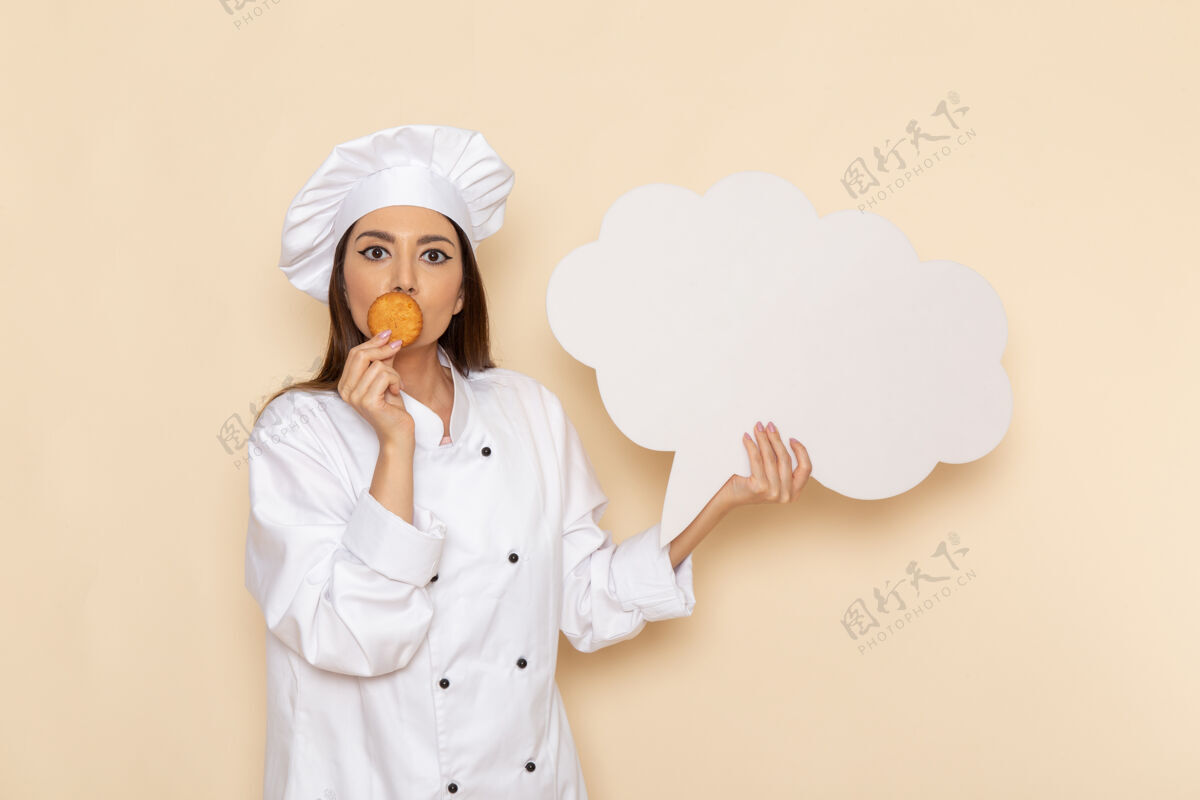 饼干身穿白色厨师服的年轻女厨师正拿着饼干和白墙上的白色标志工作女烹饪