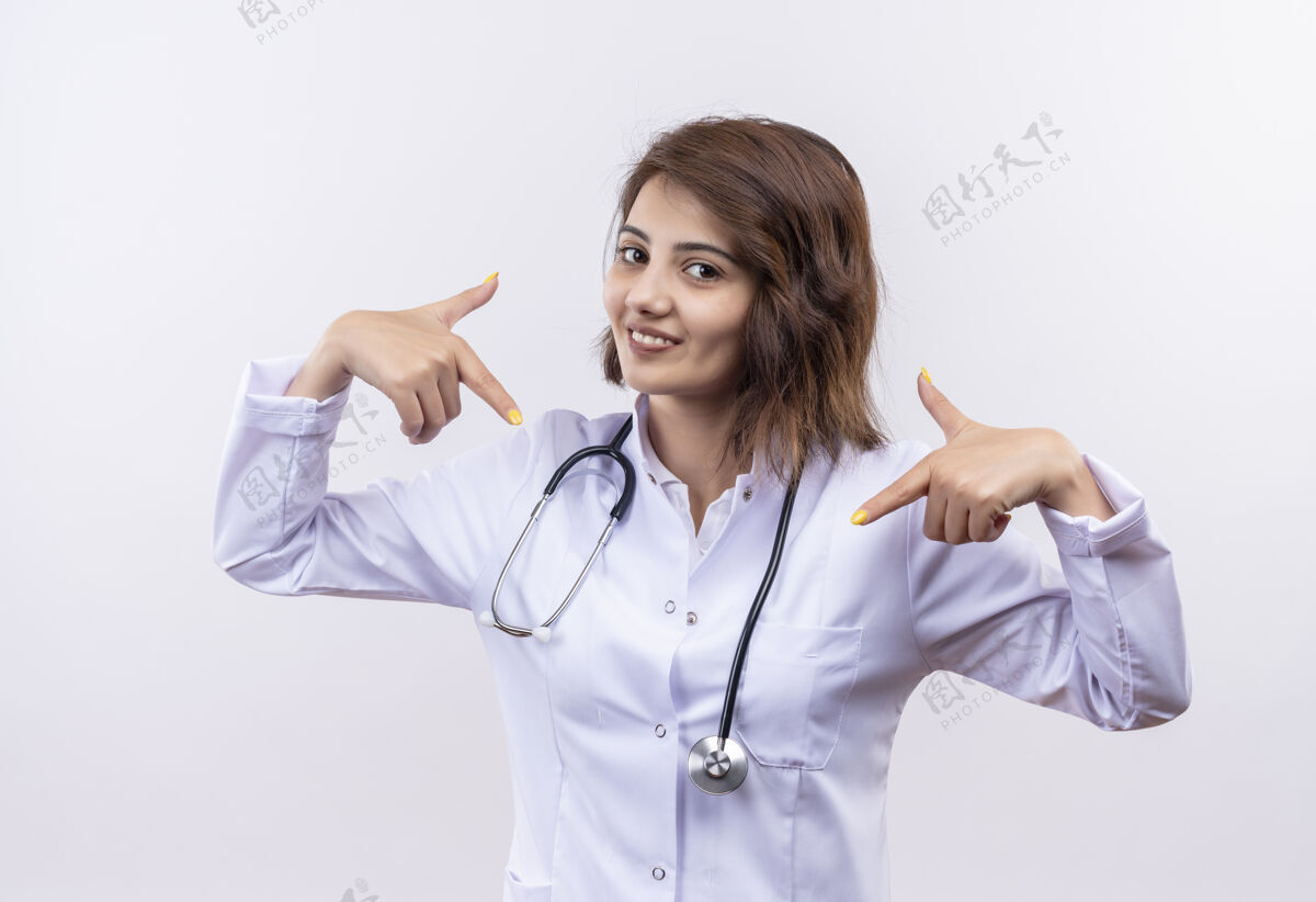 年轻人身穿白大褂 手持听诊器的年轻女医生 看上去自信满面 微笑着用手指着自己 自鸣得意而自豪站着指着医生