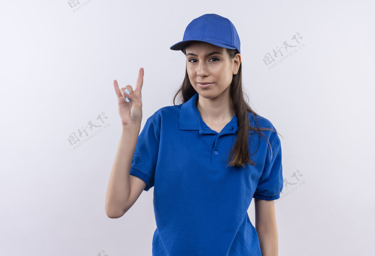 显示身穿蓝色制服 戴着帽子的年轻送货女孩自信地用手指展示摇滚乐的象征蓝色女孩交付