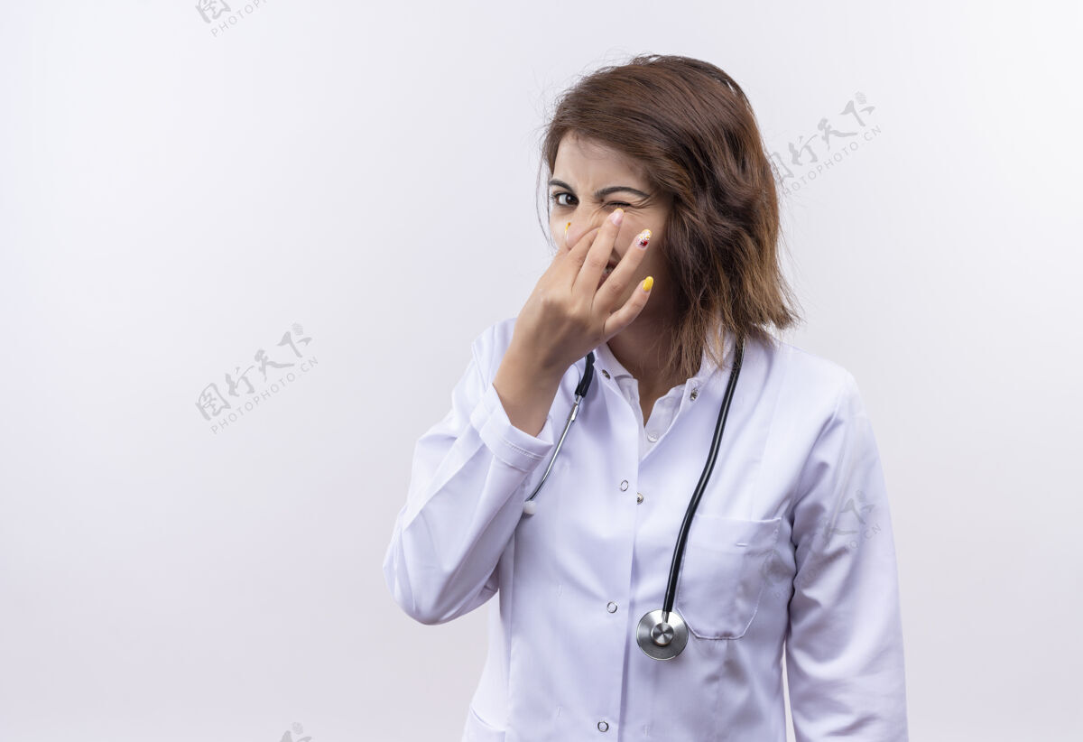 恶心穿着白大褂的年轻女医生带着听诊器闭着鼻子 表情厌恶地忍受着恶臭闭着听诊器医生