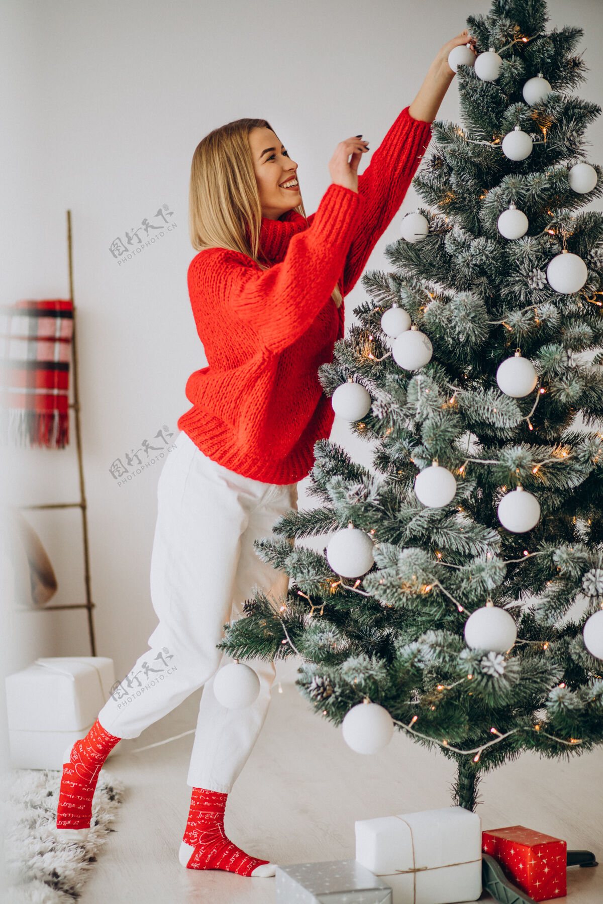 礼物装饰圣诞树的年轻女人开朗红色毛衣笑