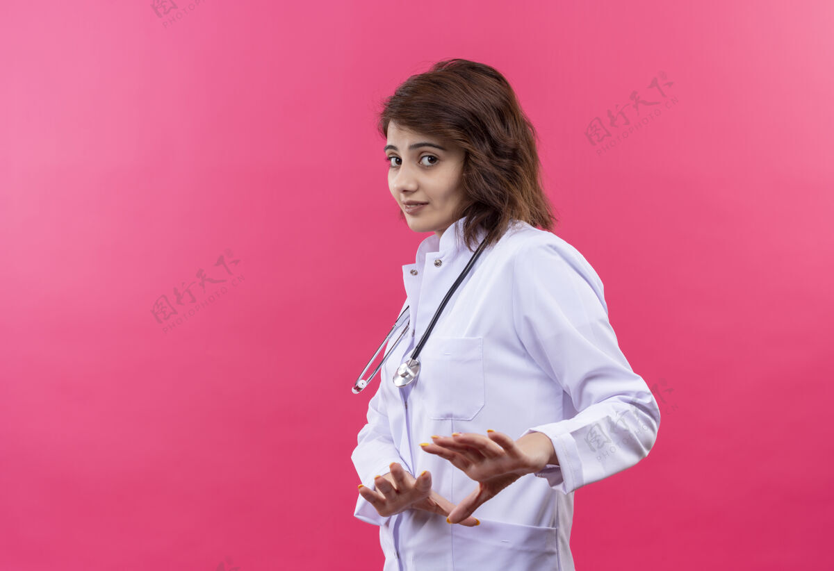 防御沮丧的年轻女医生 穿着白大褂 手持听诊器 带着厌恶的表情做着防御的手势沮丧表情年轻