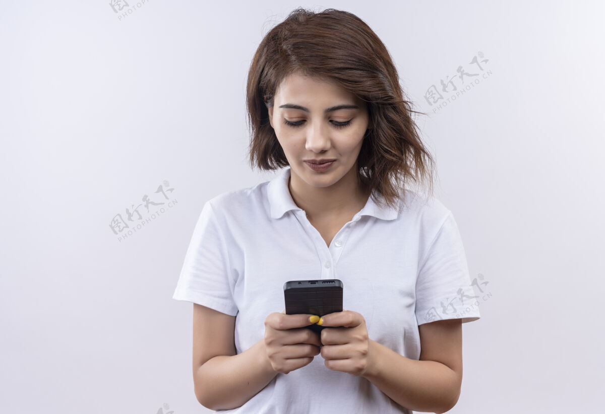 手机一个短发女孩 穿着白色马球衫 拿着手机 面带微笑地聊天聊天穿微笑
