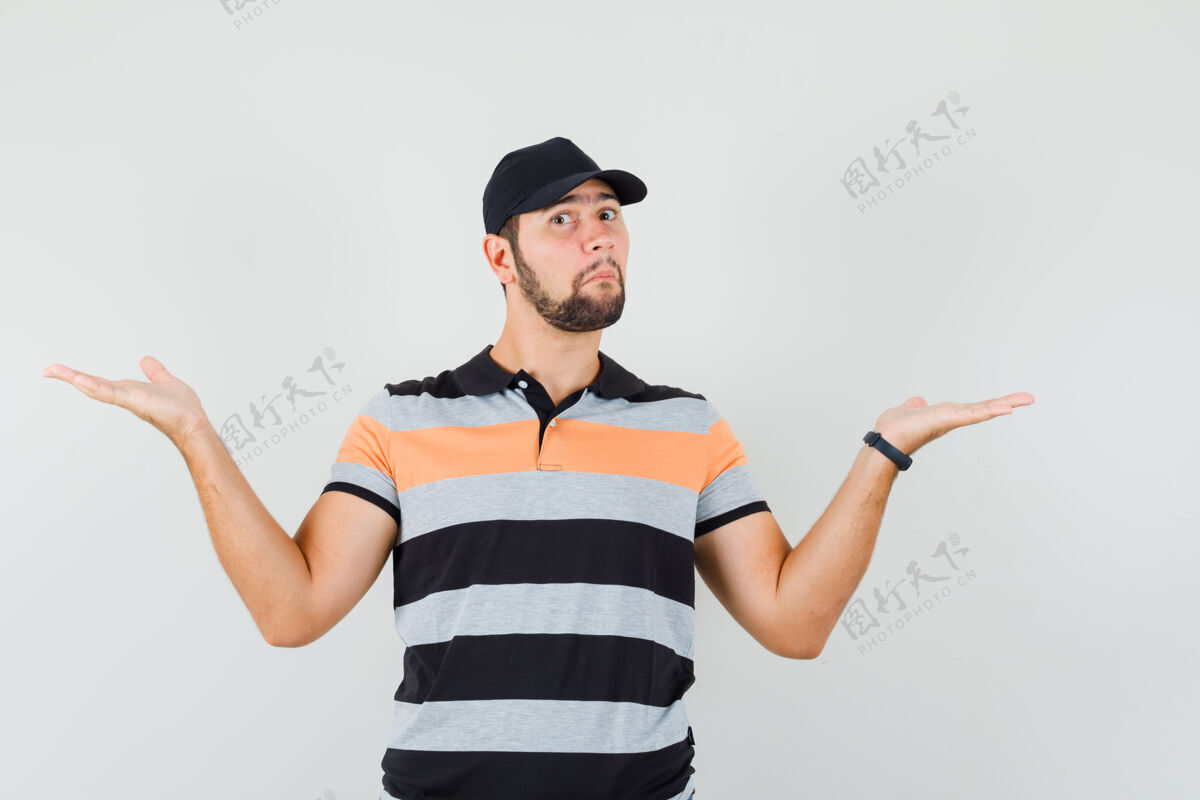 帽子一个年轻人穿着t恤 戴着帽子做着秤的手势 看上去很困惑前视图成人胡茬交叉
