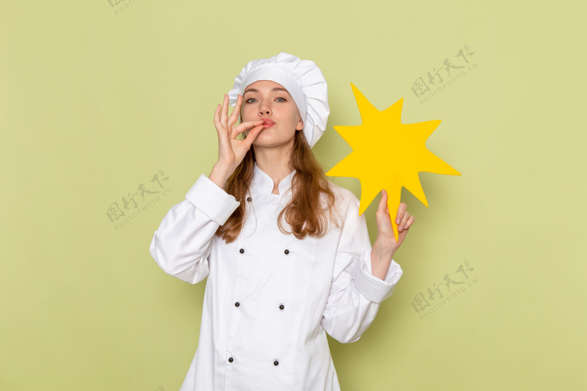 用餐女厨师身穿白色厨师服 手持绿色墙壁上的黄色标志 正视图女厨师举行微笑