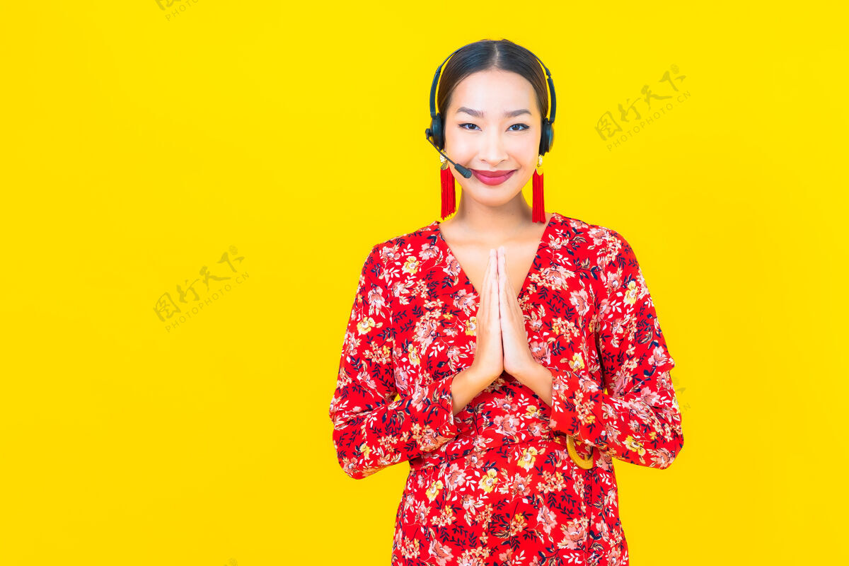 联系人在黄色墙上为客户呼叫中心护理戴着耳机的美丽亚洲年轻女子画像支持交谈帮助热线