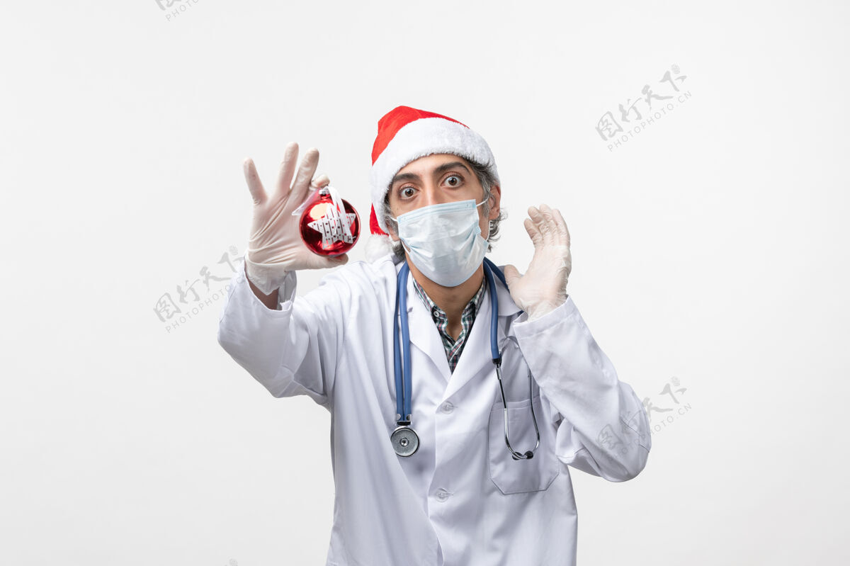 成人正面图戴面具的男医生带着玩具上了白墙健康冠状病毒新年服装病毒圣诞节