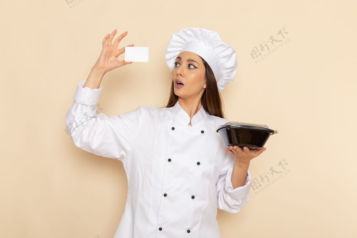 女性身穿白色厨师服的年轻女厨师在白色墙壁上拿着平底锅的正视图年轻人微笑前面