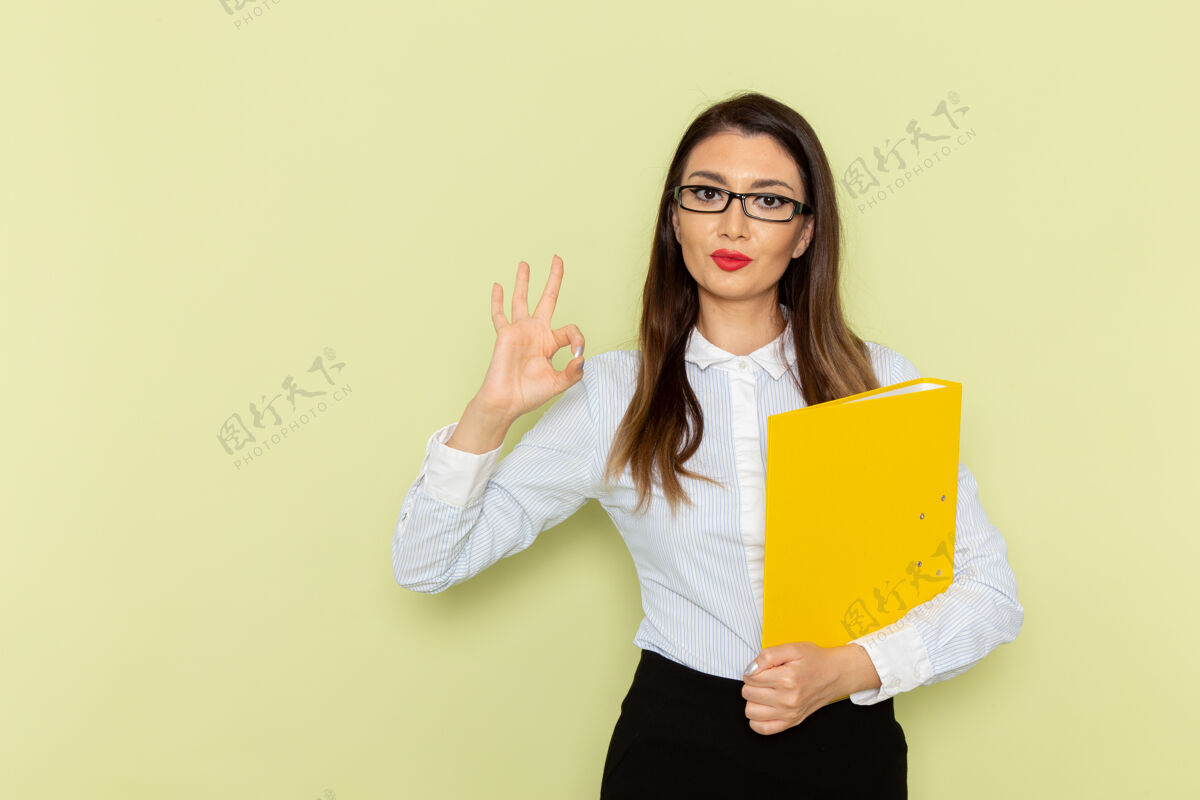 文件身穿白衬衫和黑裙子的女上班族手持黄色文件 在绿色墙上摆姿势姿势工人衬衫