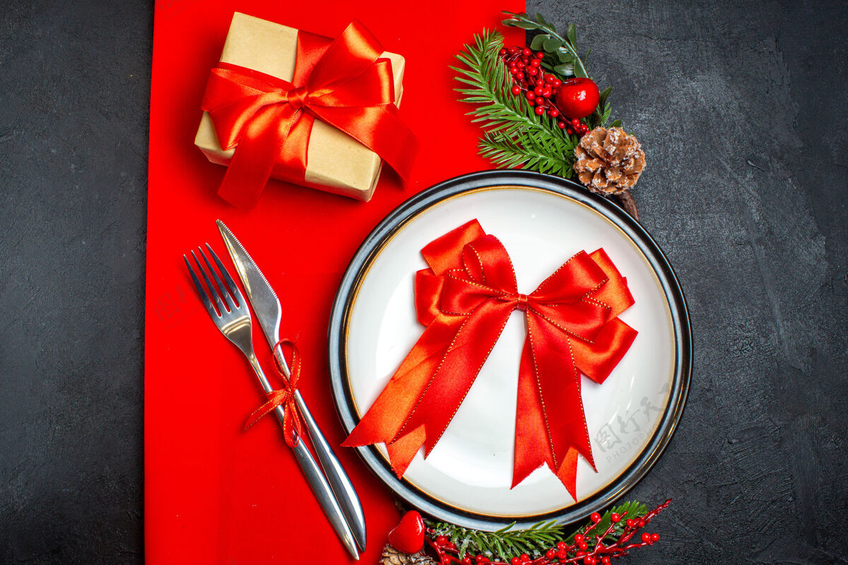 树枝顶视图新年背景上有红丝带的餐盘餐具套装装饰配件杉木树枝旁边有一个红色餐巾上的礼物顶餐盘餐巾