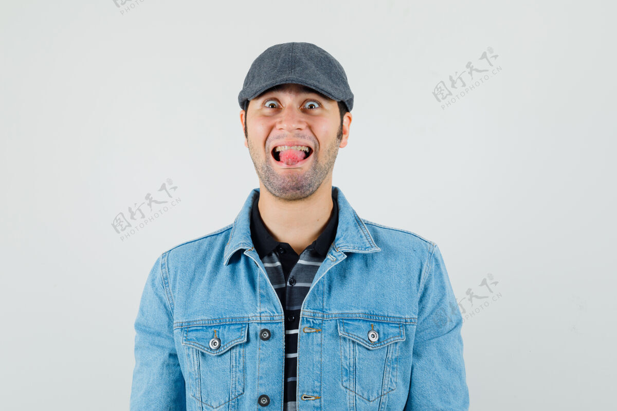 朋友戴帽子 穿t恤 穿夹克的年轻人伸出舌头 看上去很滑稽棒男自信