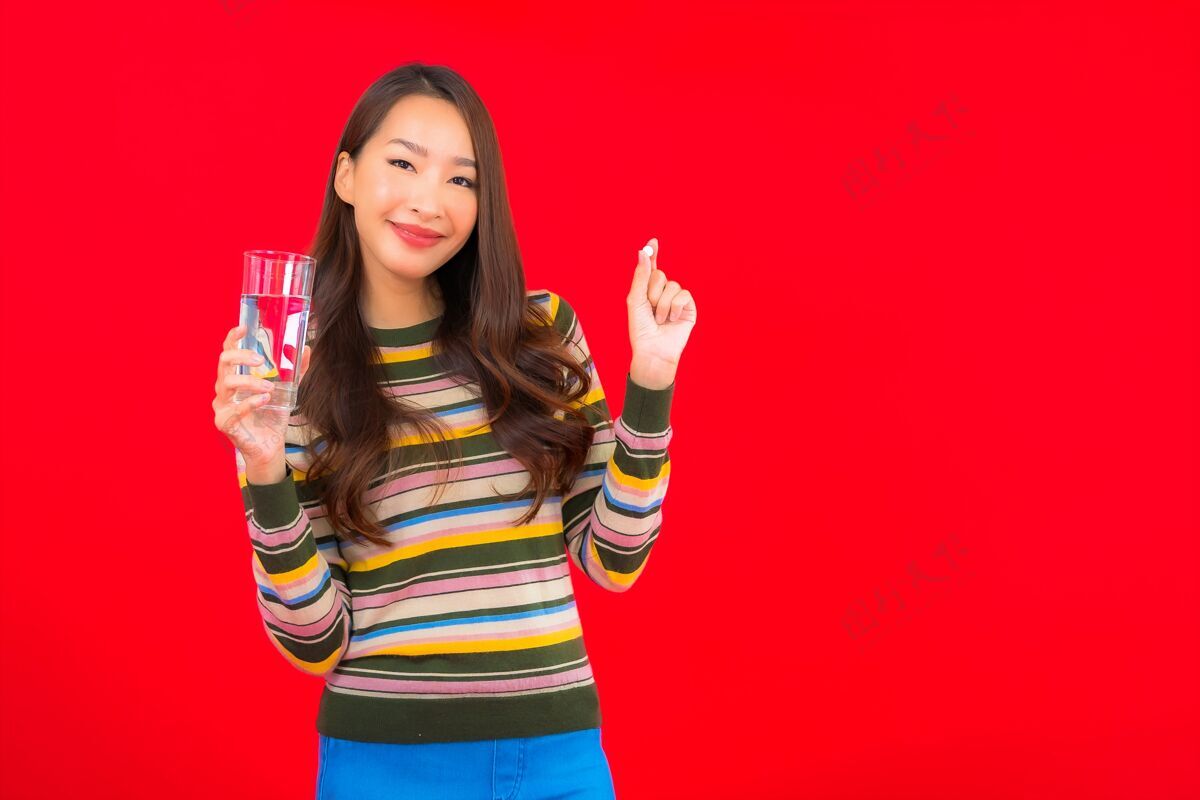 中国在红墙上画一幅美丽的亚洲年轻女子的画像 她拿着水和药丸平板香港健康