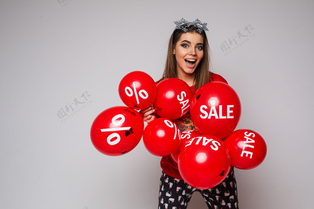 气球一张照片是一位身穿睡衣 头戴雪花眼镜 手里拿着一堆贴着减价和折扣贴纸的红色气球的激动的黑发女人的照片折扣假日雪花