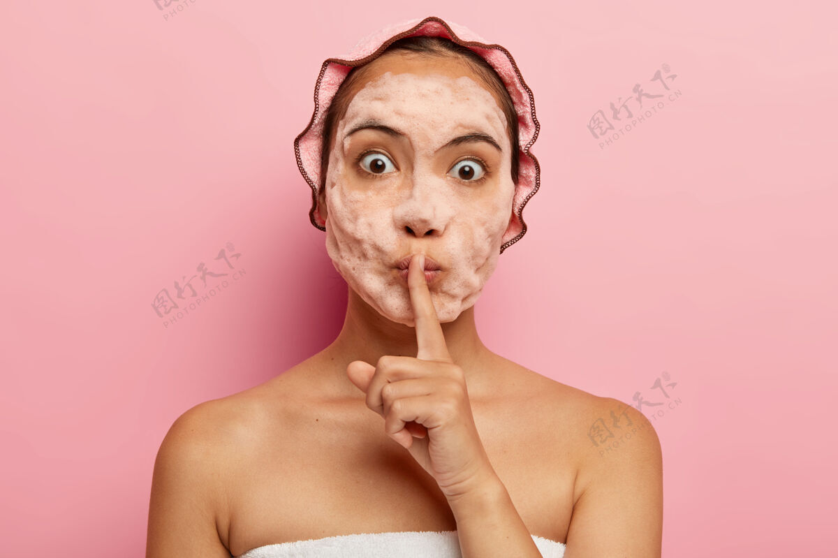 清洁惊讶的韩国女士的形象 脸上有肥皂泡 做沉默的手势 告诉美丽的秘密 清洁和去角质的皮肤 在空闲时间有美容程序 照顾自己人震惊卫生