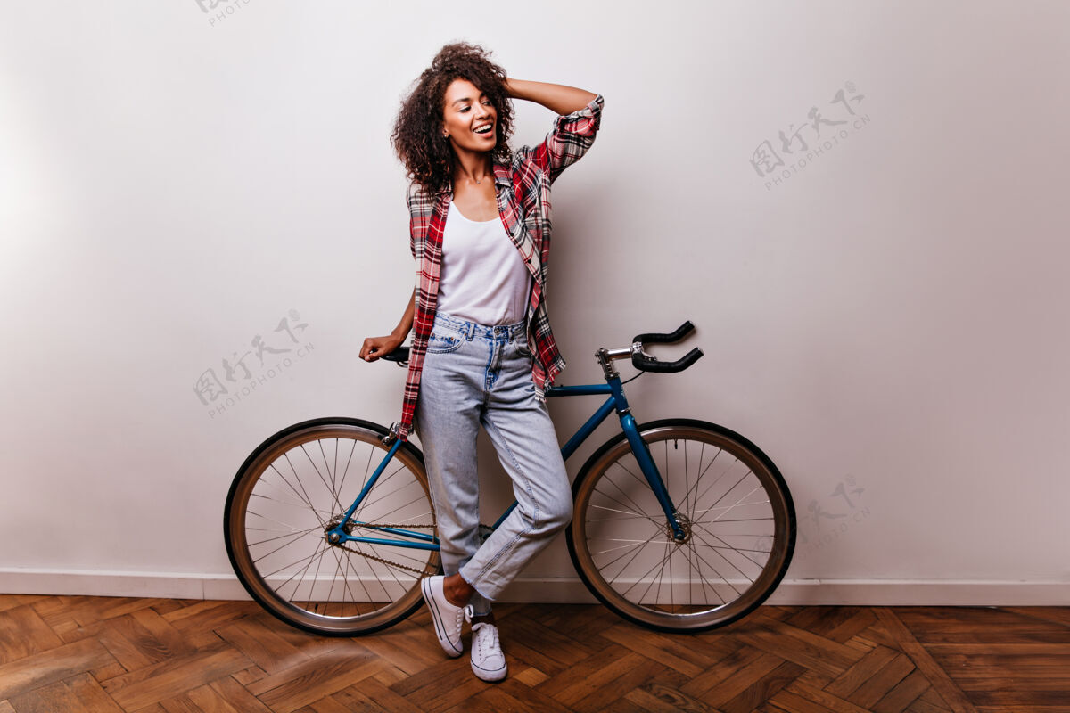 活跃骑自行车的漂亮卷发女士的全长镜头乐观的黑人女孩在摆姿势时抚摸着她的头发黑发积极美国黑人
