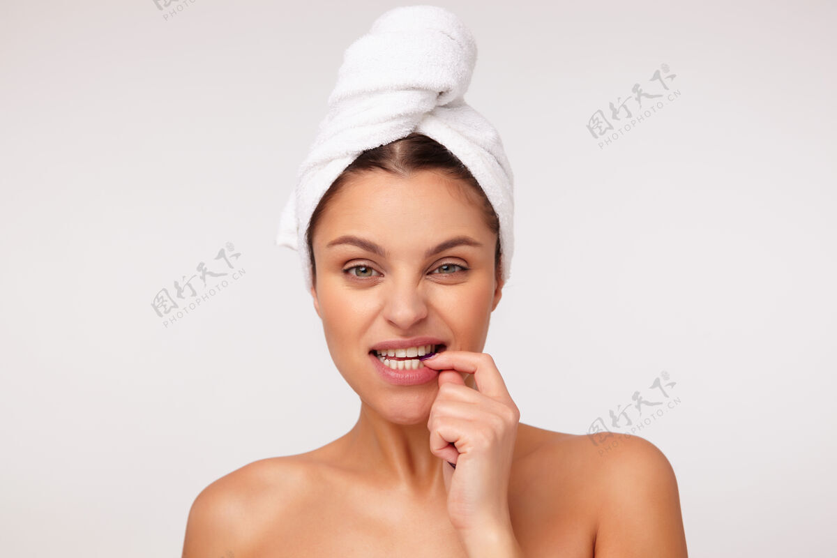 女人一幅年轻可爱的黑发女性的肖像 头上戴着毛巾 皱着眉头 咬着手指 看着镜头 在白色背景下赤裸着肩膀摆姿势年轻食指情绪