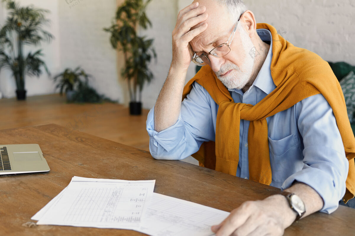过度工作照片中是一位压力重重 心烦意乱的成熟白人商人 穿着正式的衣服 戴着眼镜 坐在打开的笔记本电脑前 研究文件 面对财务问题 手放在光头上办公桌老人疲惫