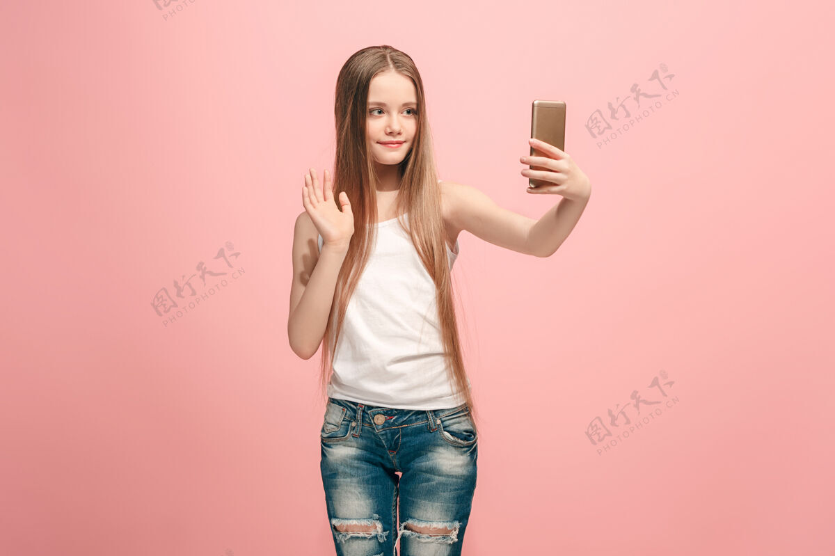 面部快乐的少女站着 粉色的微笑 用手机自拍人类的情感 面部表情的概念教育人乐趣