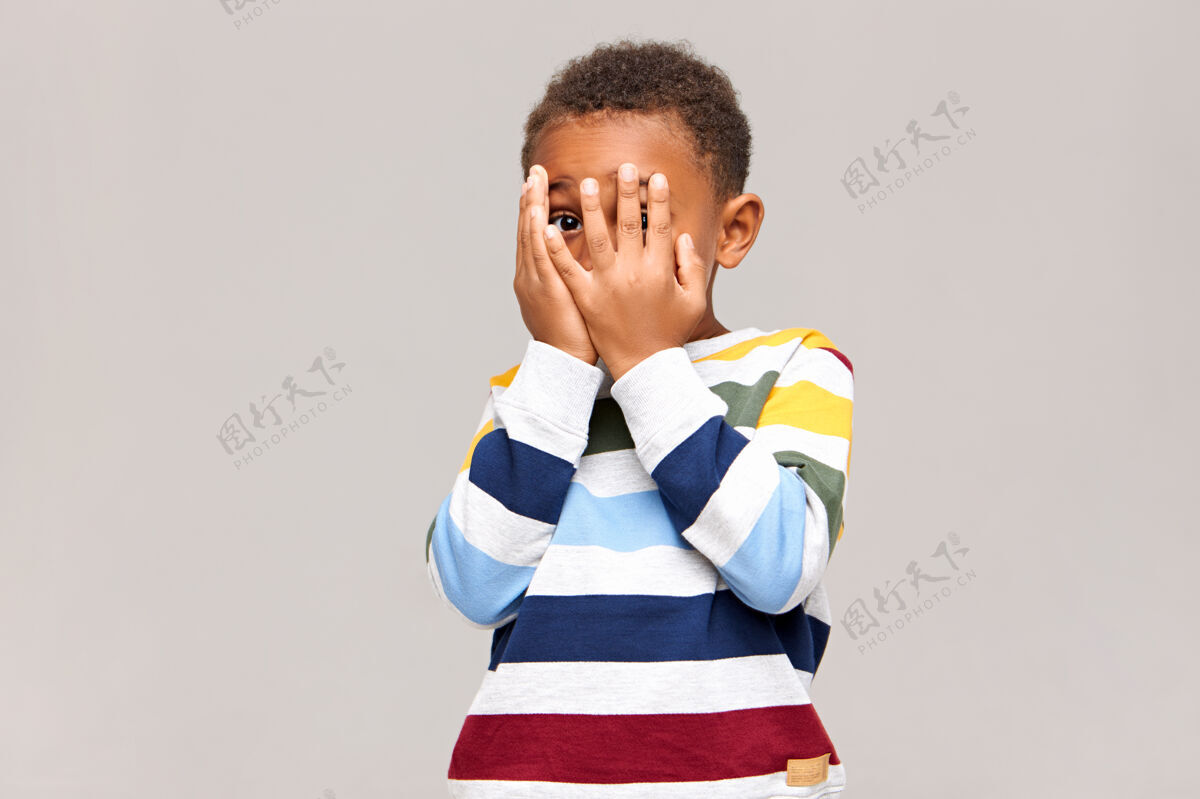 肖像害怕的黑皮肤小男孩用双手捂着脸 好像害怕看到什么可怕的东西 从指间的洞里窥探害羞的非洲孩子躲起来 或者玩捉迷藏羞耻隐藏哭泣