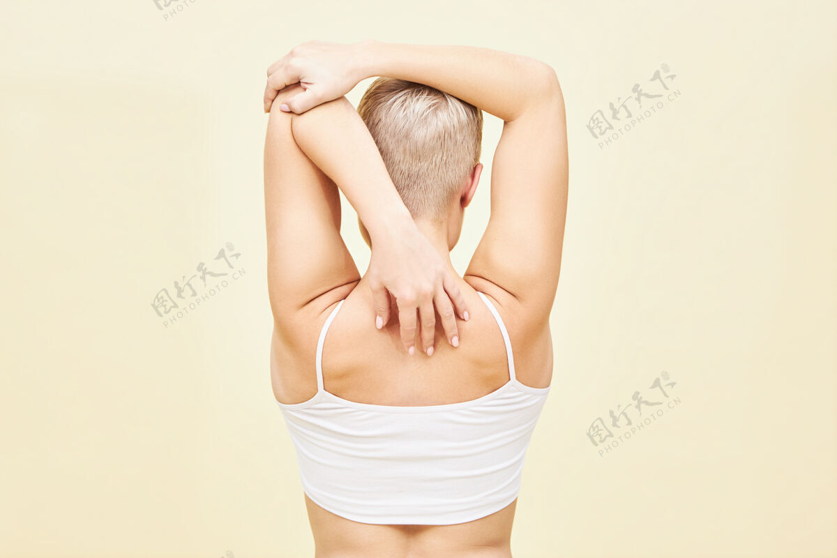 女人无法辨认的年轻女子的后视图 男孩般的短发向后伸展手臂 提高肩关节的活动性 打开胸部人 运动和健身理念后方年轻运动
