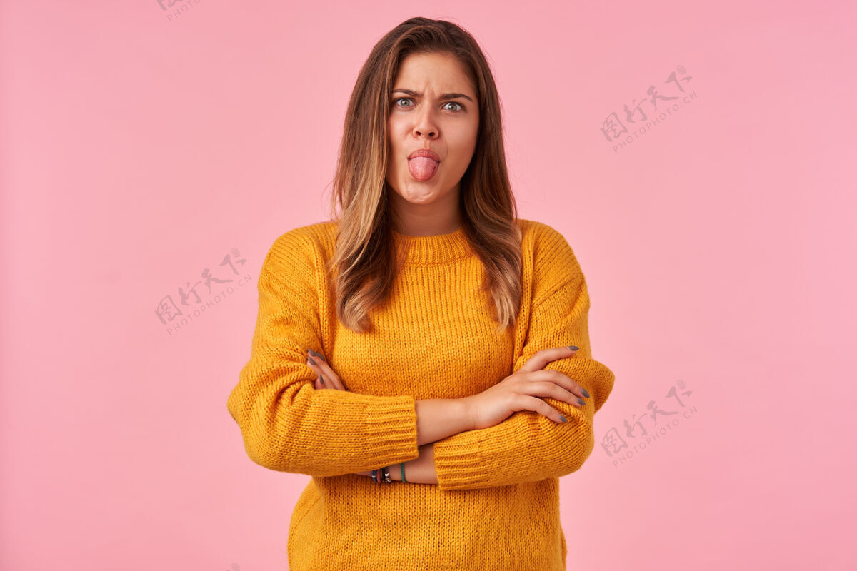 面部室内画像年轻漂亮的黑发女性折叠双手放在胸前和愚弄 而在粉红色的姿势 皱眉和显示舌头衣服室内情绪