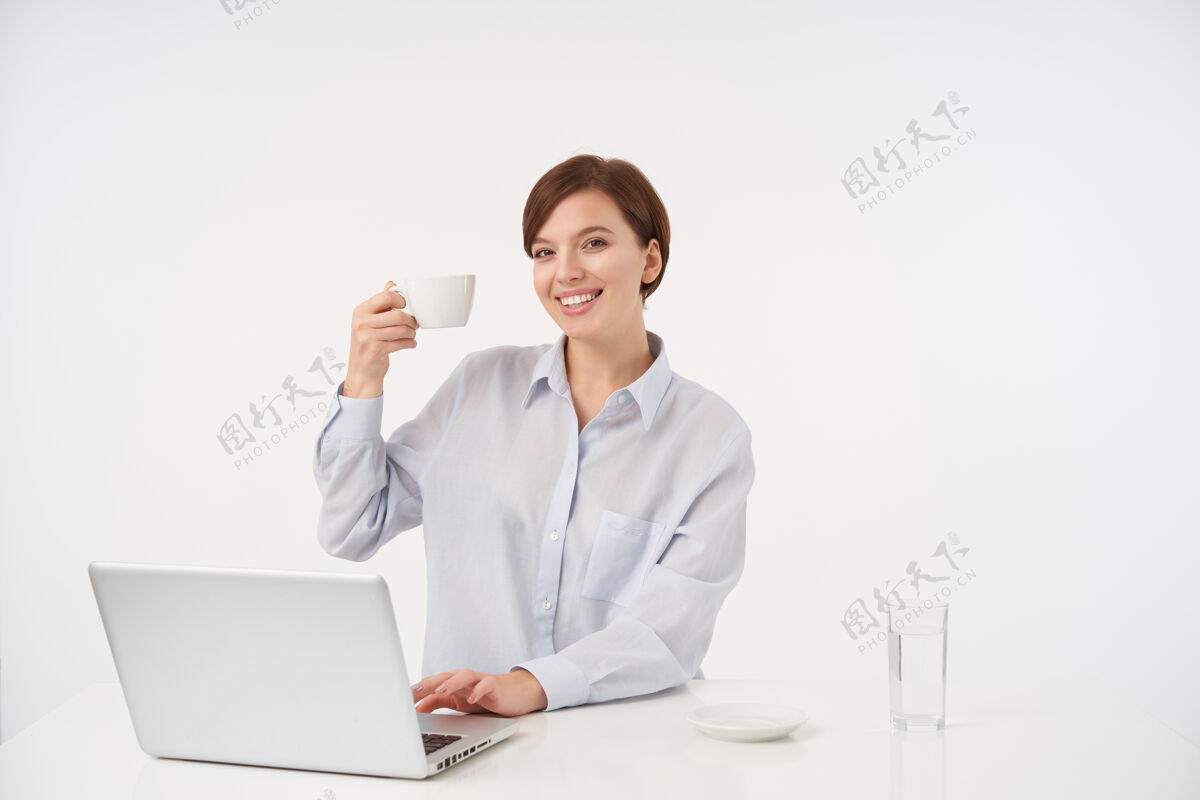 休闲快乐年轻美丽的棕色头发的女人 自然化妆 举起手 端着一杯茶 面带迷人的微笑 愉快地坐在白色的椅子上女商人女性工作