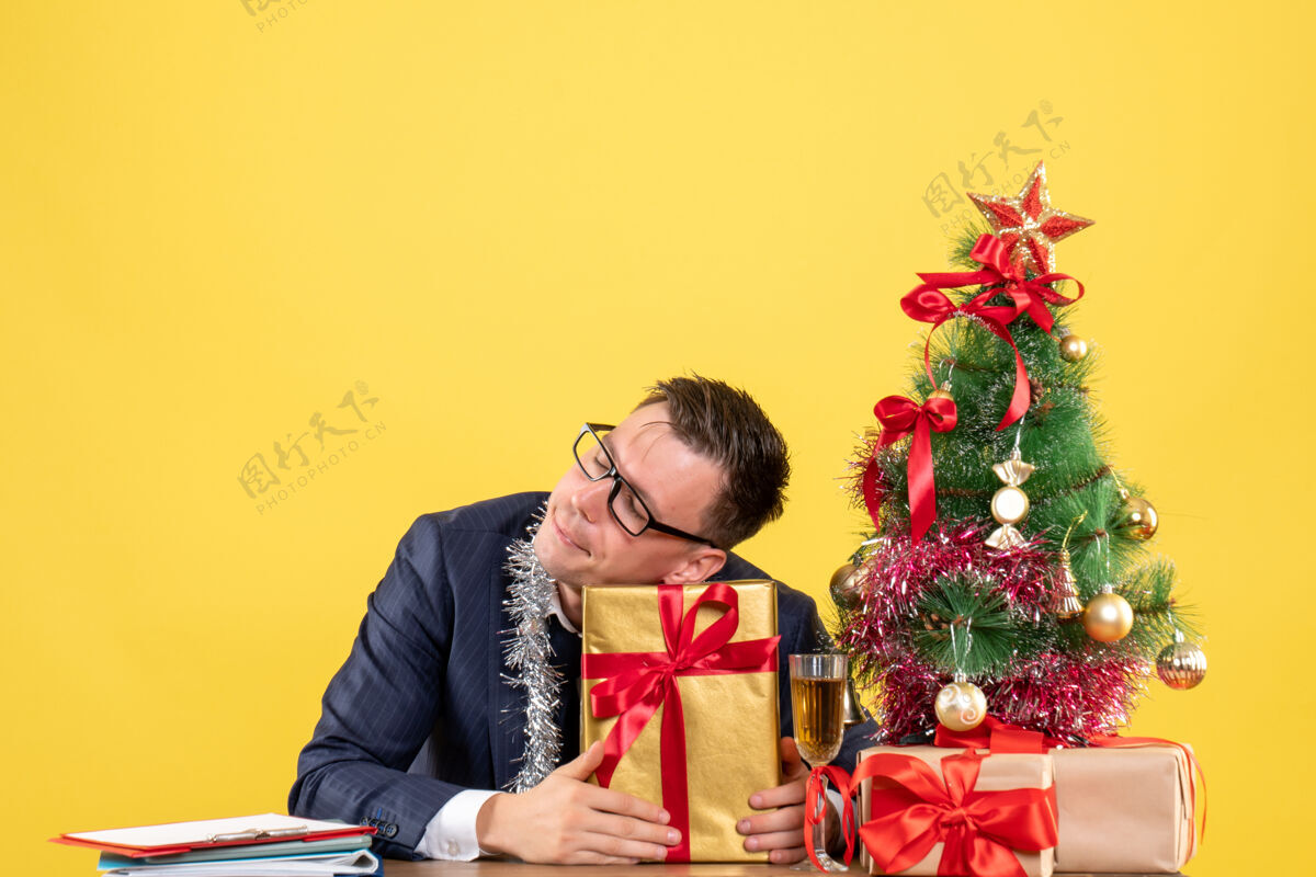 礼物帅哥拿着礼物坐在圣诞树旁的桌子前 黄色的礼物礼物男人桌子