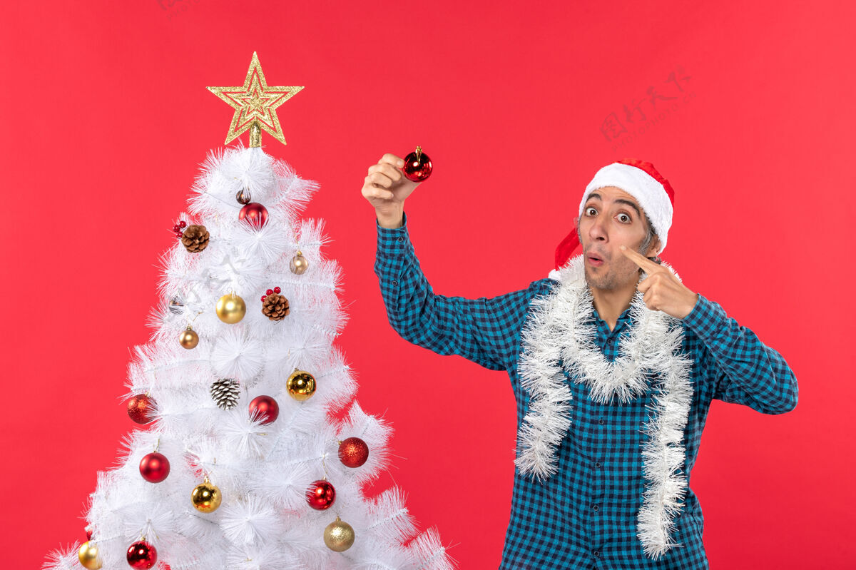 圣诞树一个带着圣诞老人帽子 穿着蓝色条纹衬衫 满脸笑容 情绪化 滑稽可笑的年轻人庆祝男人圣诞