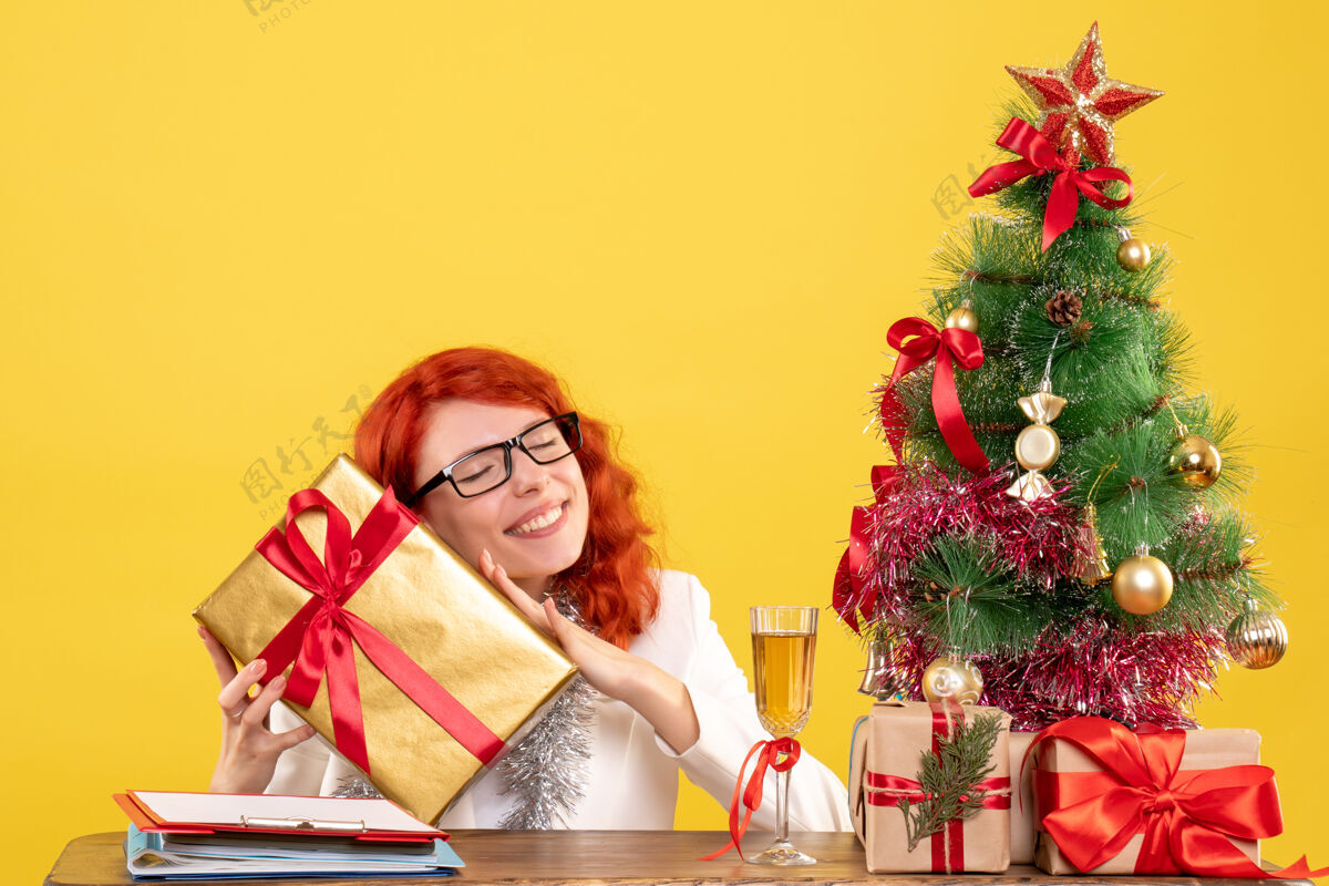 肖像前视图：女医生坐在黄色背景上 手里拿着圣诞礼物和圣诞树女情感树