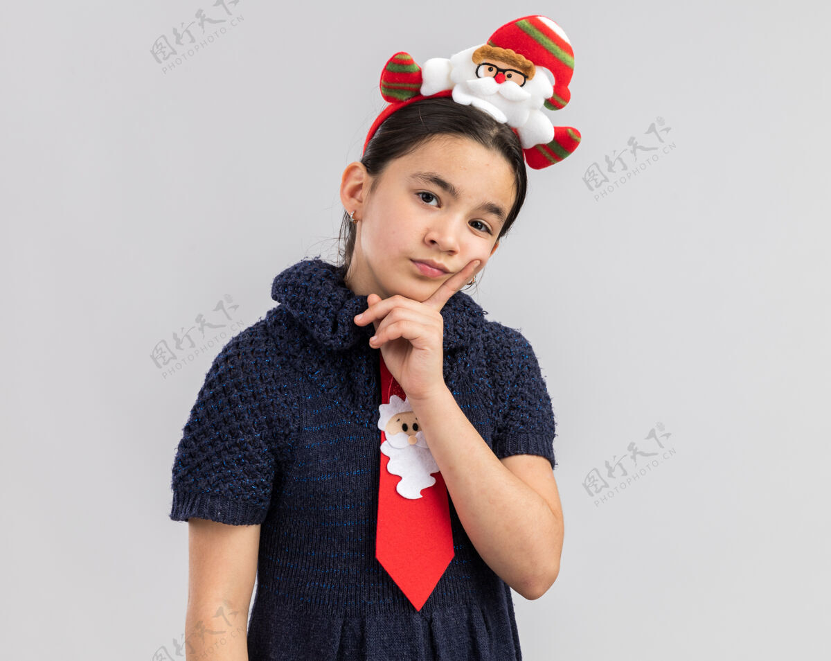 搞笑穿着针织连衣裙的小女孩头上戴着一条红色领带 上面戴着一个滑稽的圣诞边 看上去很困惑红快乐圈