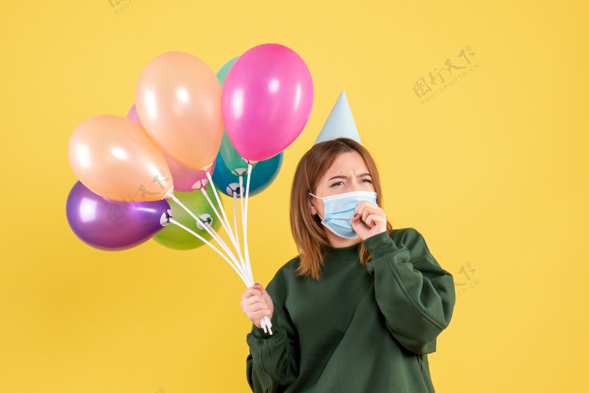 节日正面图戴面具的年轻女性手持五颜六色的气球生日年轻的女性病毒