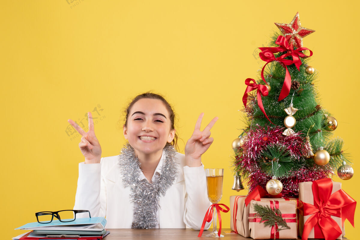 前面前视图女医生围坐在圣诞礼物和圣诞树摆姿势与黄色背景上的微笑花女性树