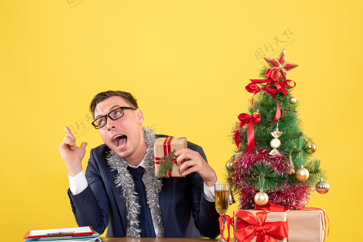 礼物手持礼物的神秘人坐在圣诞树旁的桌子前 黄色的礼物礼物成人套装