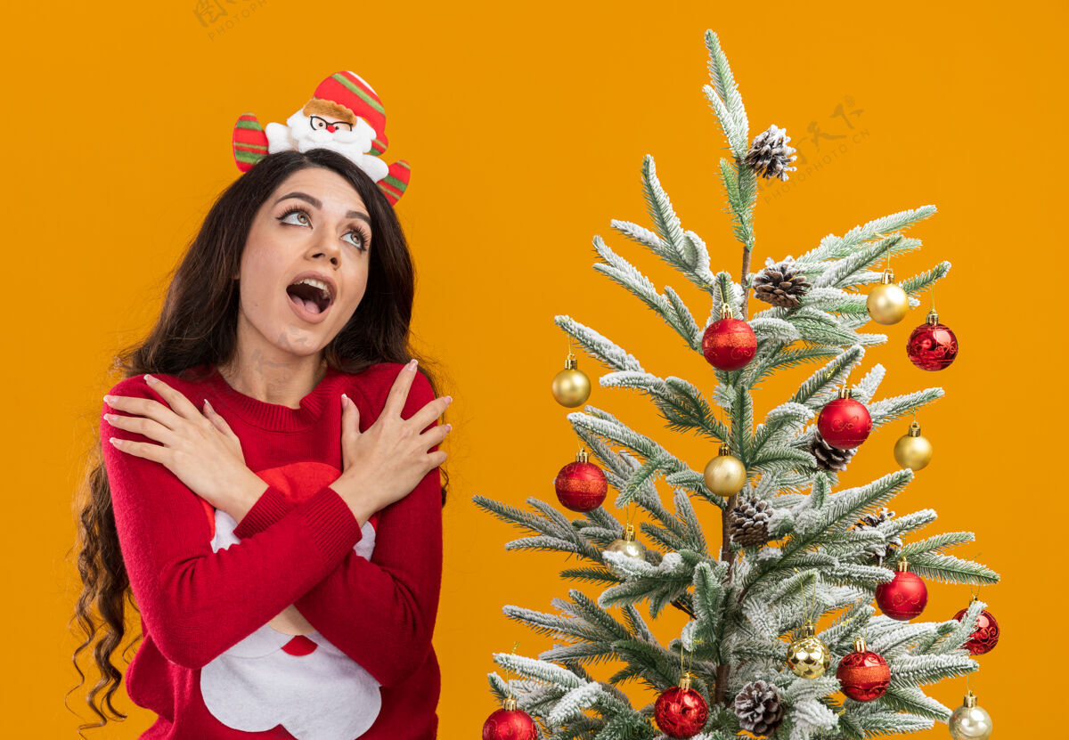 手兴奋的年轻漂亮女孩戴着圣诞老人的头带和毛衣站着圣诞节女孩