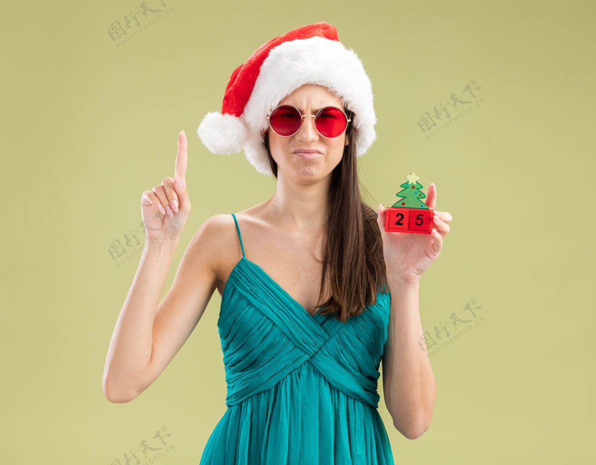 女孩戴着太阳眼镜 戴着圣诞帽 拿着圣诞树饰物 指着头的年轻白人女孩复制圣诞快乐年轻