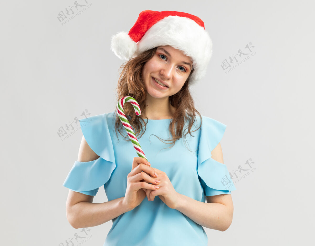 高兴身穿蓝色上衣 戴圣诞帽 手持糖果手杖的年轻女子 面带微笑年帽子站着