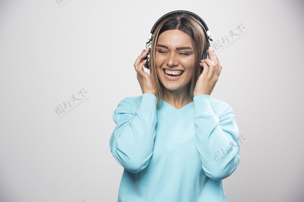 服装穿着蓝色运动衫的金发女孩戴着耳机 享受着音乐和乐趣摆姿势喜欢人类
