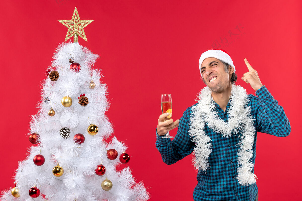 庆典情绪喜剧快乐有趣的年轻人 戴着圣诞老人的帽子 穿着蓝色的衬衫 手里拿着一杯葡萄酒杯子圣诞圣诞老人
