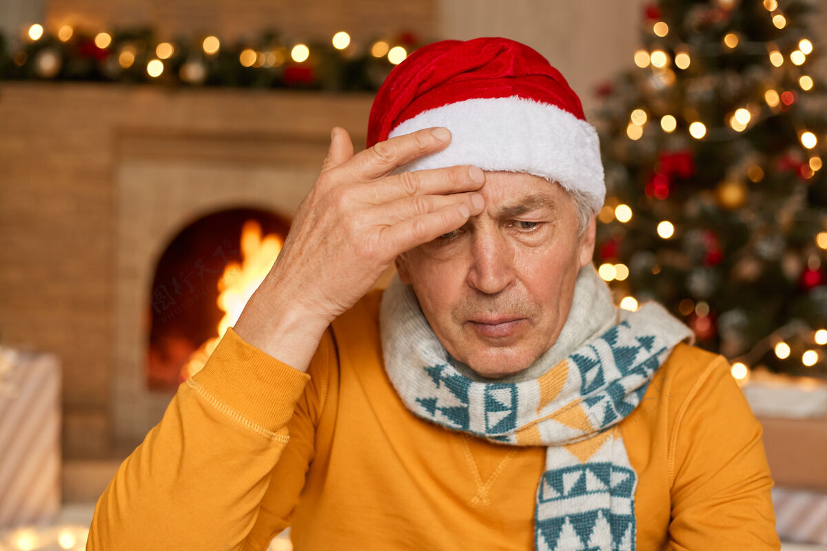 老年人成熟的男人在室内对着壁炉和装饰过的冷杉树摆姿势困倦天圣诞节