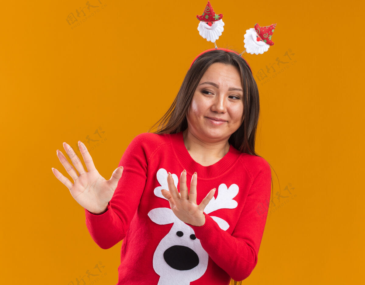 女人一个神经质的亚洲女孩 戴着圣诞发箍 手里拿着毛衣 站在橙色的墙上年轻人箍毛衣