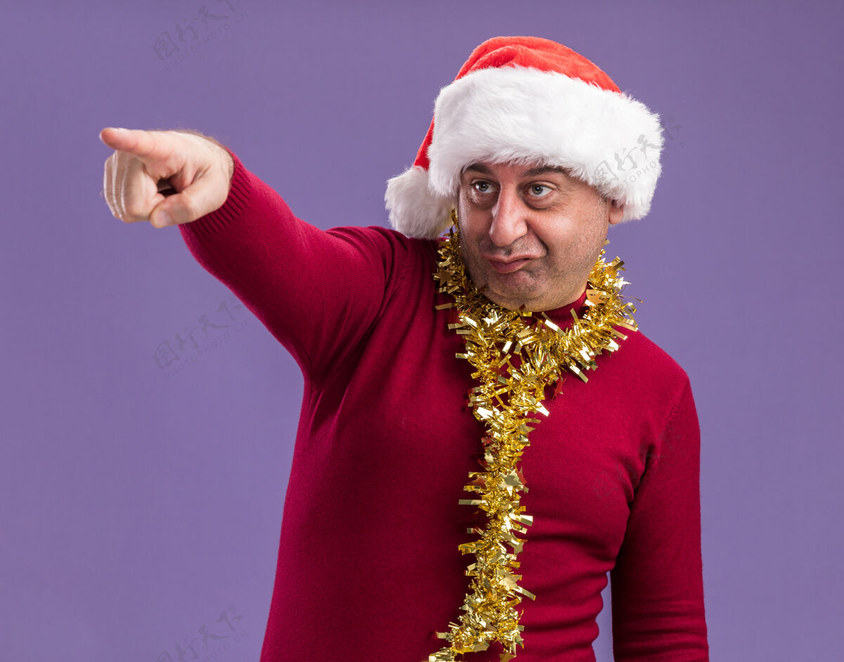 非常中年男子戴着圣诞老人的帽子 脖子上戴着金属丝 指着旁边的指南针 站在紫色的背景上感到困惑和焦虑周围站着困惑