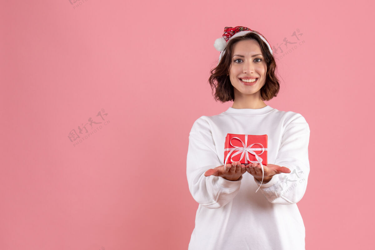 成人前视图的年轻女子举行小圣诞礼物在粉红色的墙壁微笑情感人