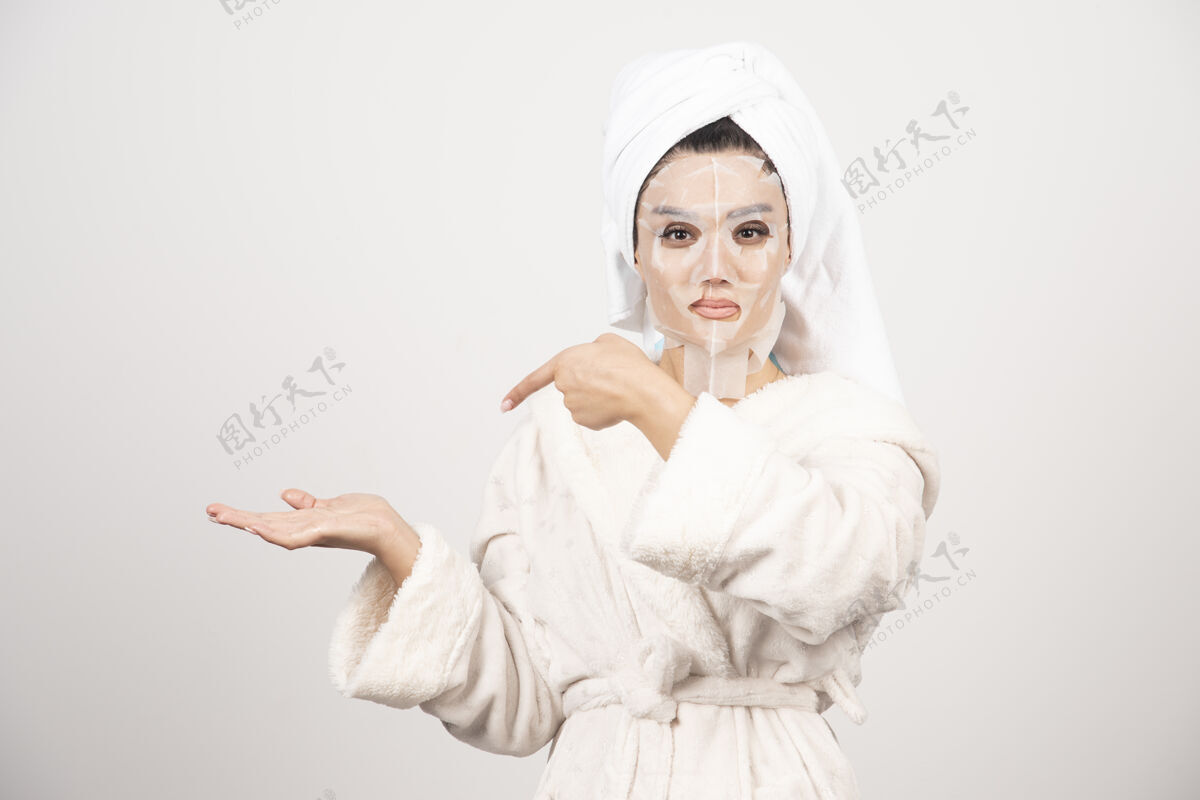 水疗穿着浴衣和带面罩的毛巾的女人漂亮面膜白色