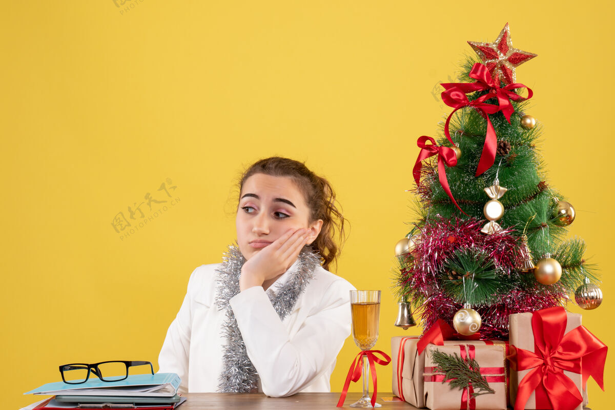 礼物前视图女医生围坐在圣诞礼物和黄色背景上的树悲伤圣诞节悲伤医生