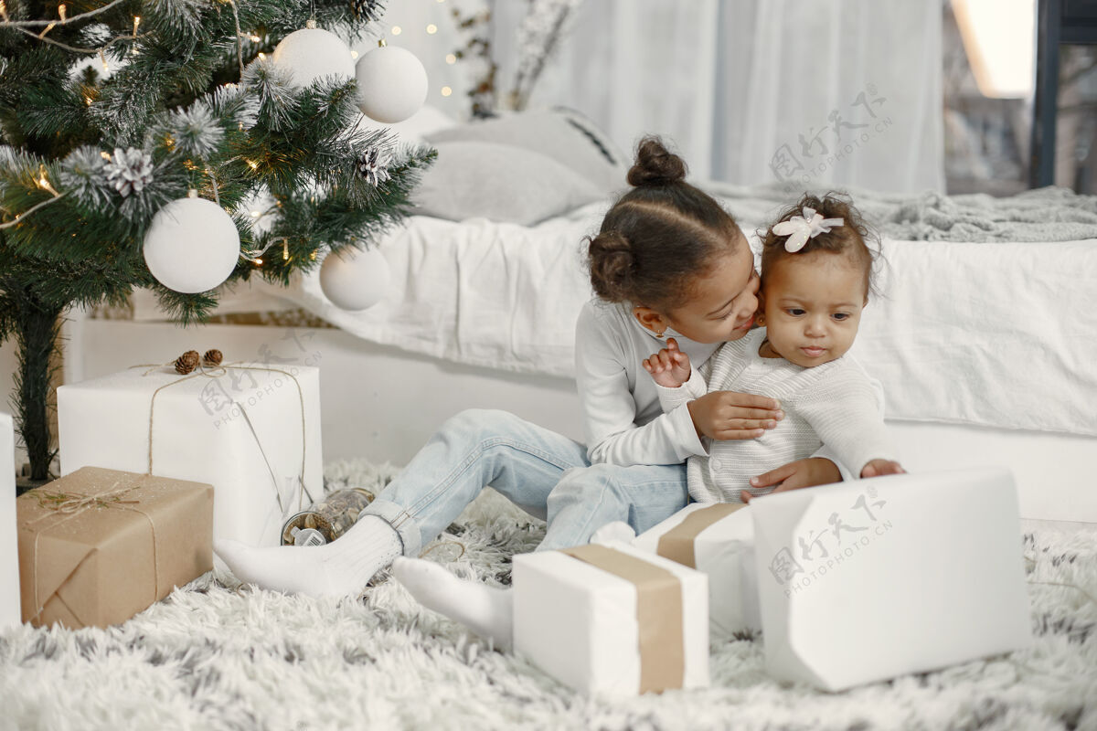 传统穿着白色毛衣的孩子女儿们在圣诞树旁缝线两个姐妹在家礼物家肖像
